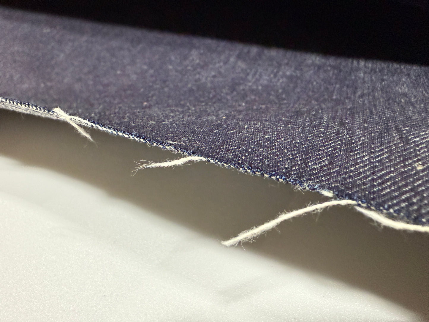 Okayama Denim 13 oz indigo kibata Japanese selvage denim fabric close-up showing raw edge and texture.
