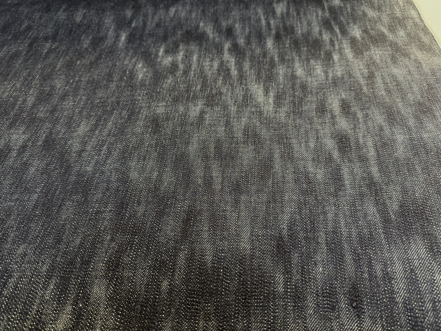 Okayama Denim fabric close-up showing the unevenly dyed texture of 16.5oz Japanese indigo slab selvage denim.