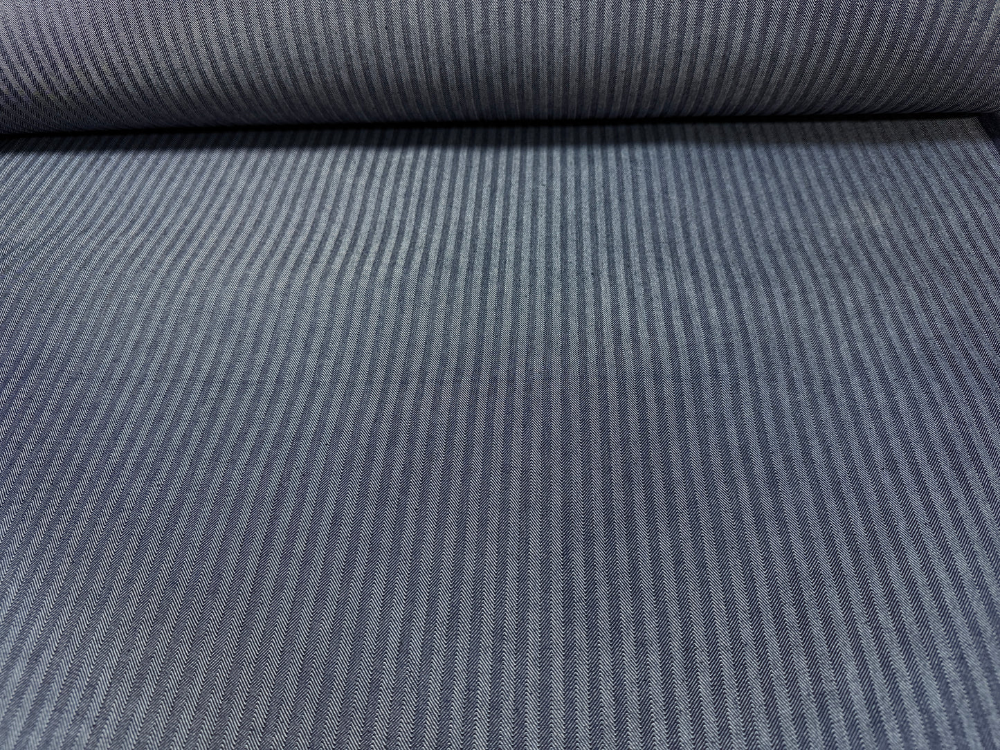 Okayama Denim fabric showing navy herringbone stripe pattern on a roll, 10.5 oz Japanese cotton material.