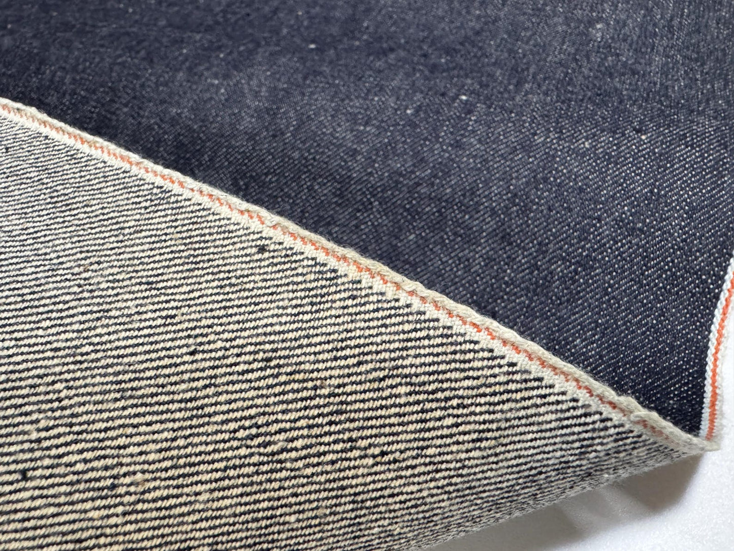 Okayama Denim | 13 oz Indigo Kibata Japanese selvage denim fabric showcasing raw texture and orange selvage edge.