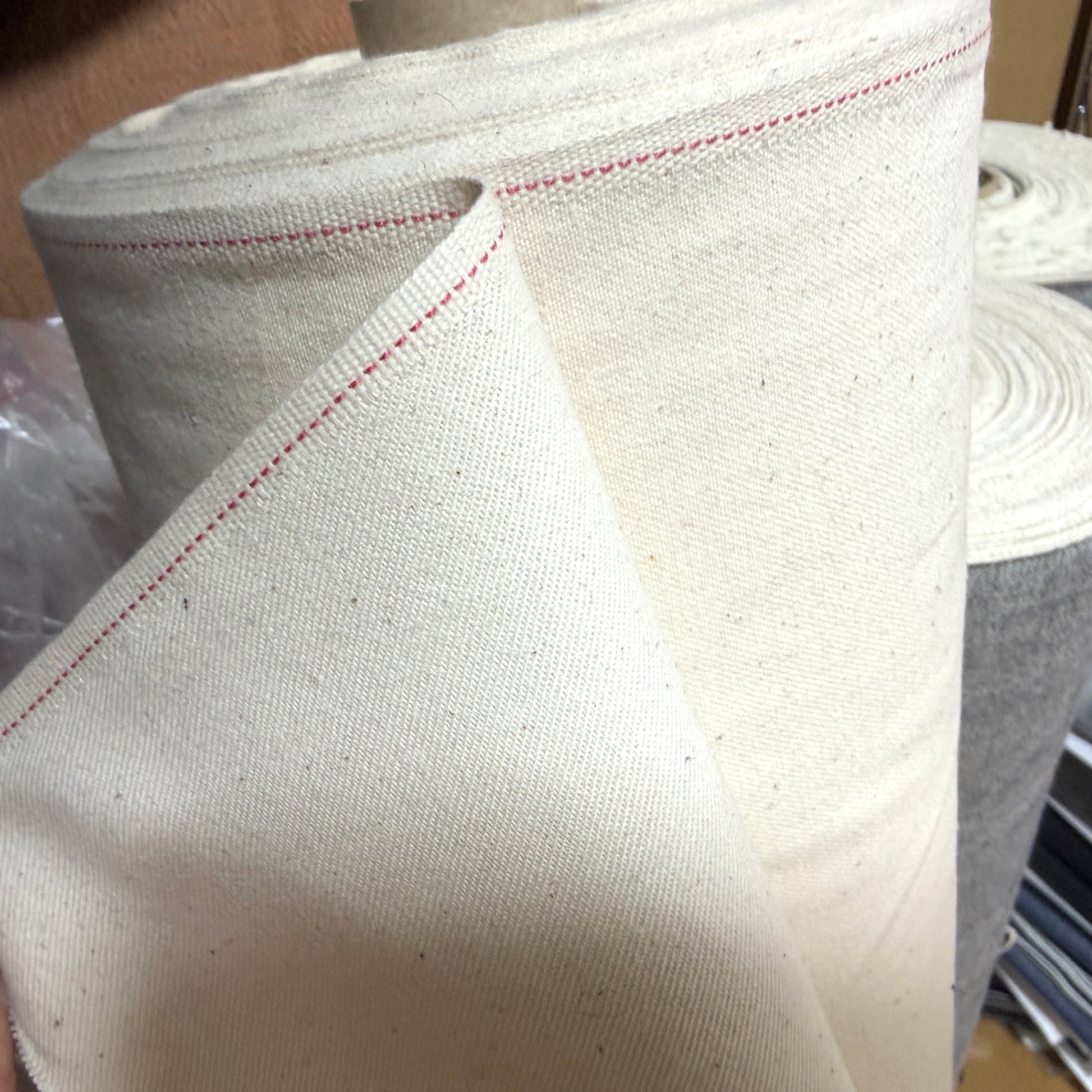 Okayama Denim cotton slake fabric rolls showcasing unbleached natural color with red stitching detail.