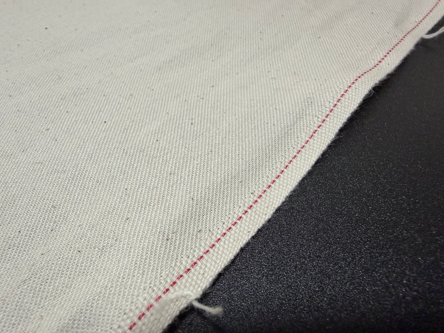 Okayama Denim slake fabric for jeans pockets showcasing natural cotton color and red stitching detail.