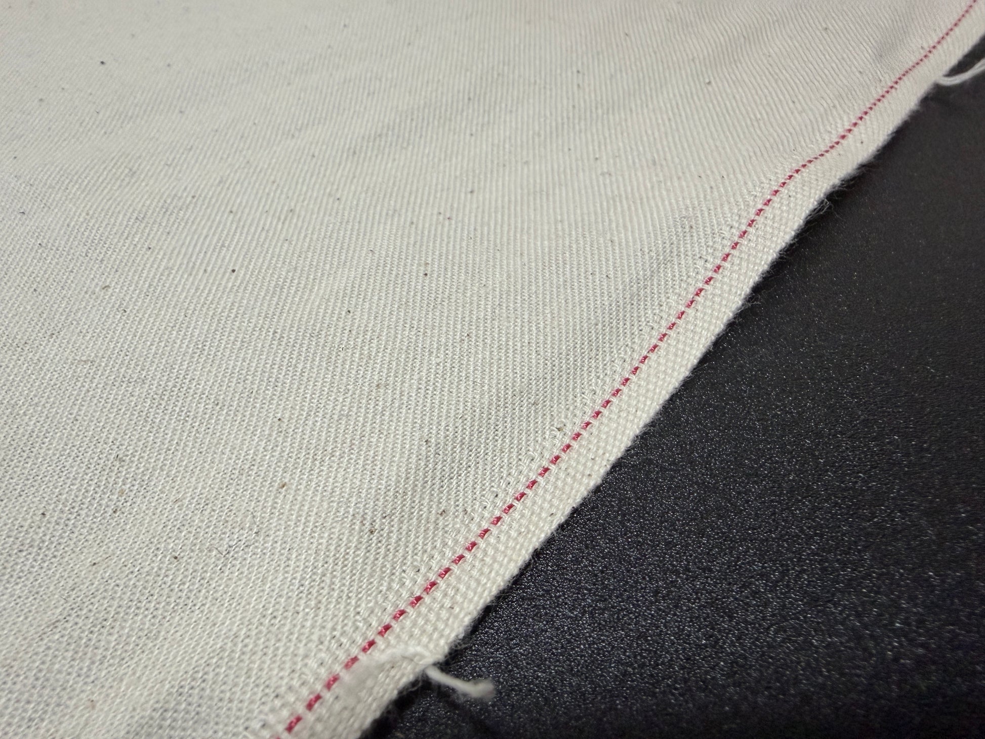 Okayama Denim slake fabric for jeans pockets showcasing natural cotton color and red stitching detail.