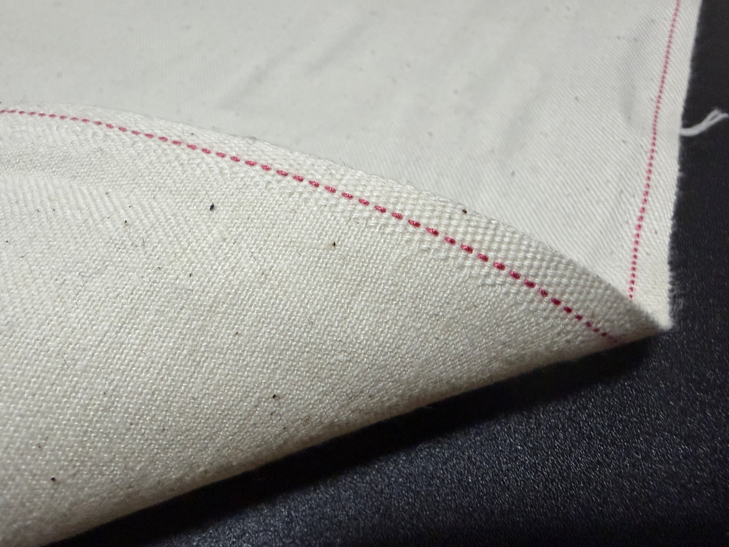 Okayama Denim cotton slake fabric showcasing unbleached color and red stitching details.