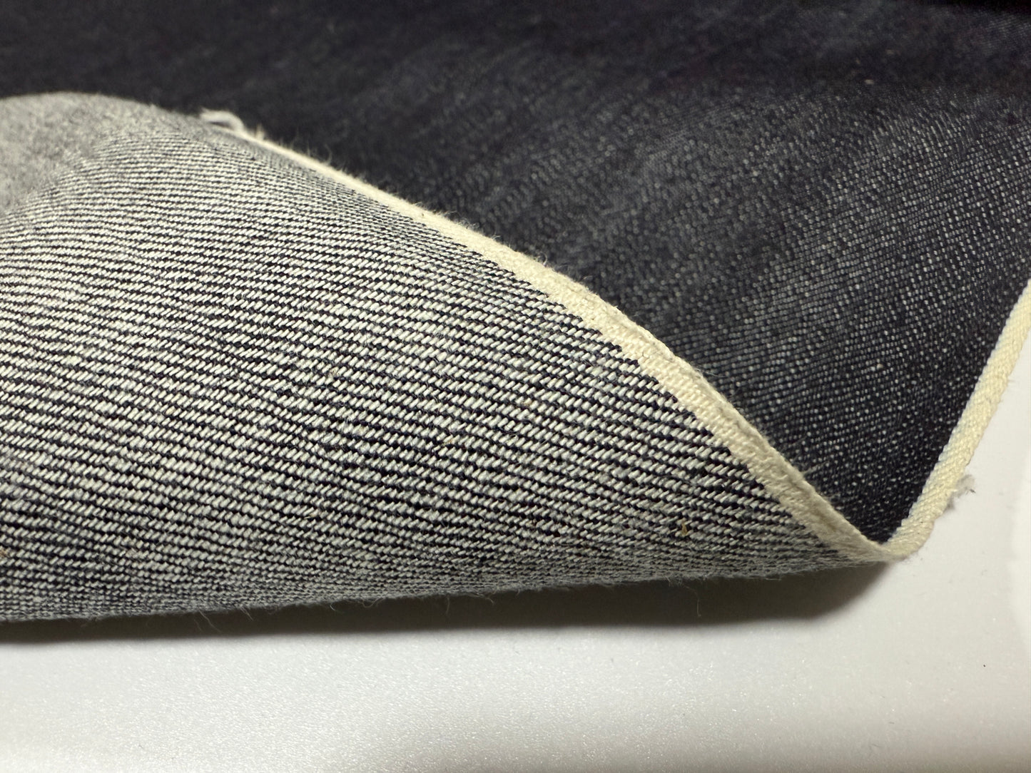 Okayama Denim showing 12.5 oz indigo Japanese selvage denim fabric with white selvage detail.