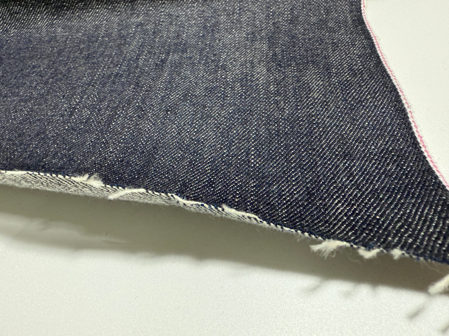 Close-up of Okayama Denim 13.5oz indigo kibata Japanese selvage fabric showcasing its raw texture and pink selvage.