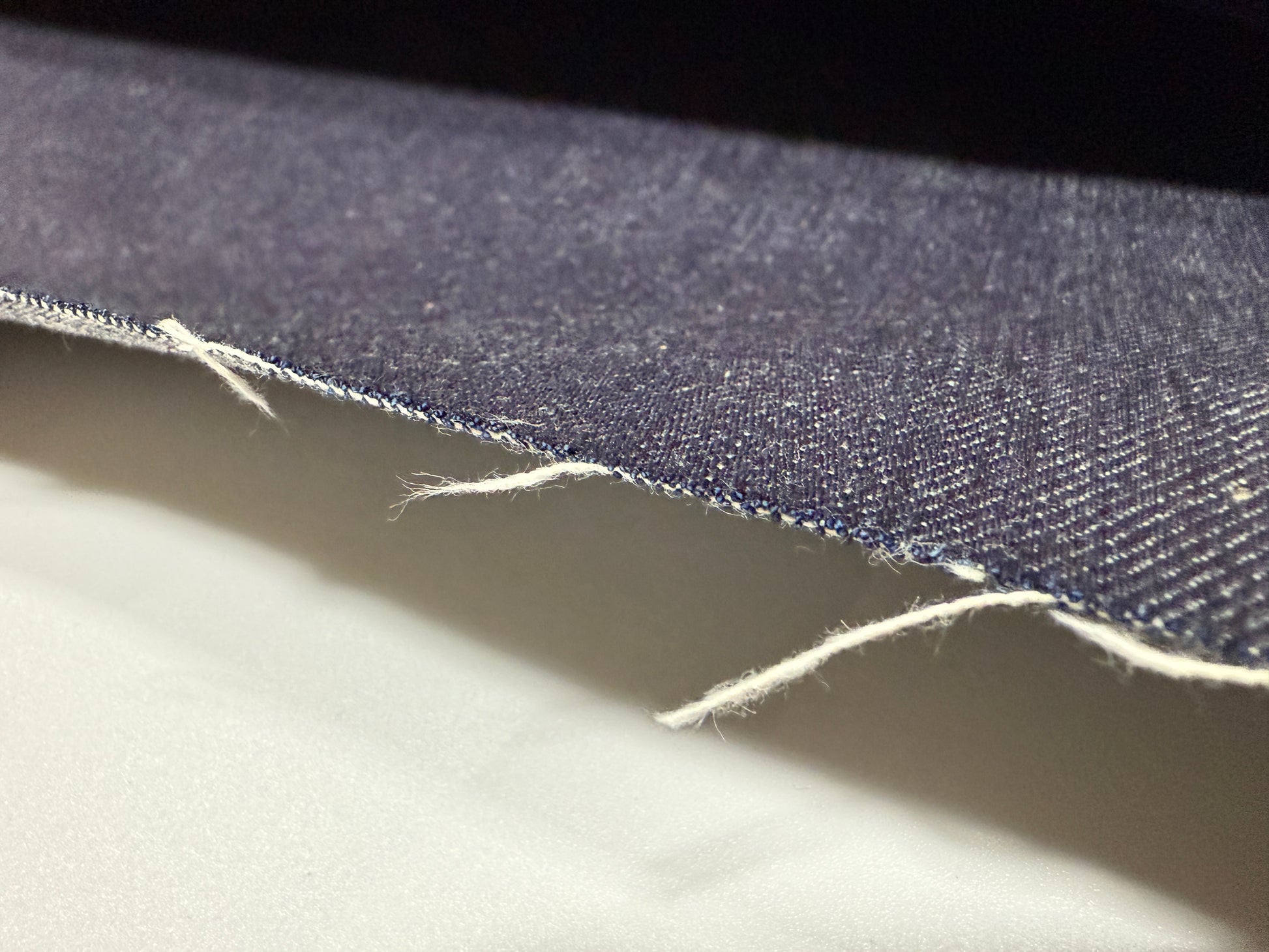 Okayama Denim 13 oz indigo kibata Japanese selvage denim fabric close-up showing raw edge and texture.