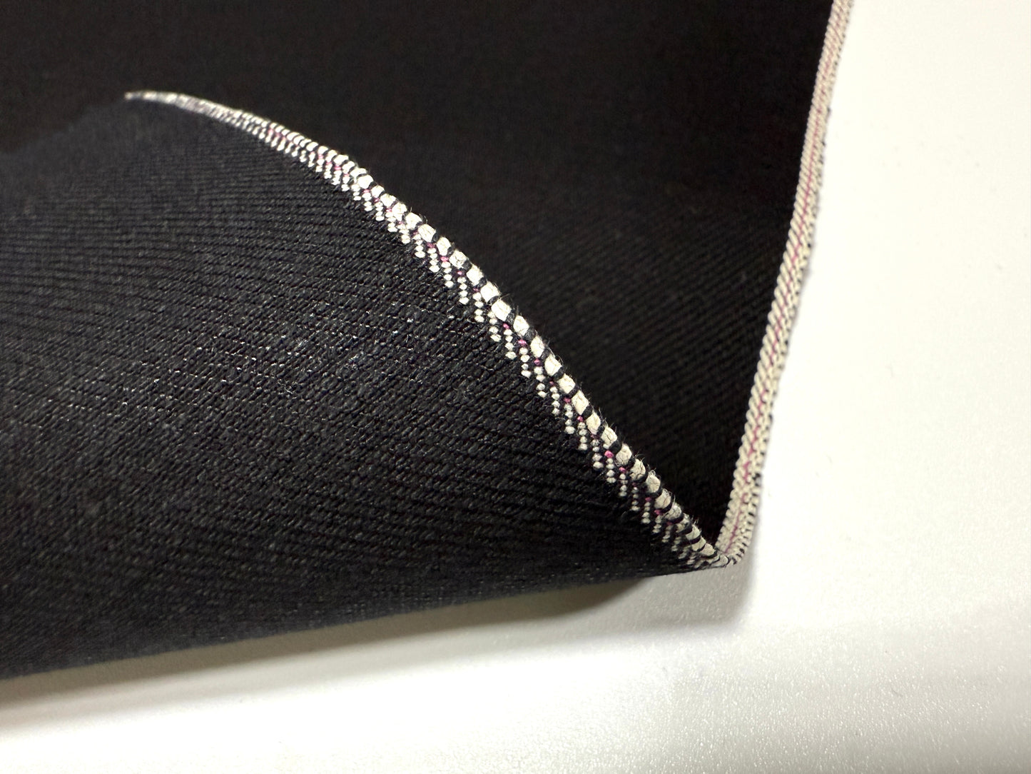 Okayama Denim | 14.6oz double-sided black Japanese selvage fabric showcasing a smooth texture and distinctive edge.