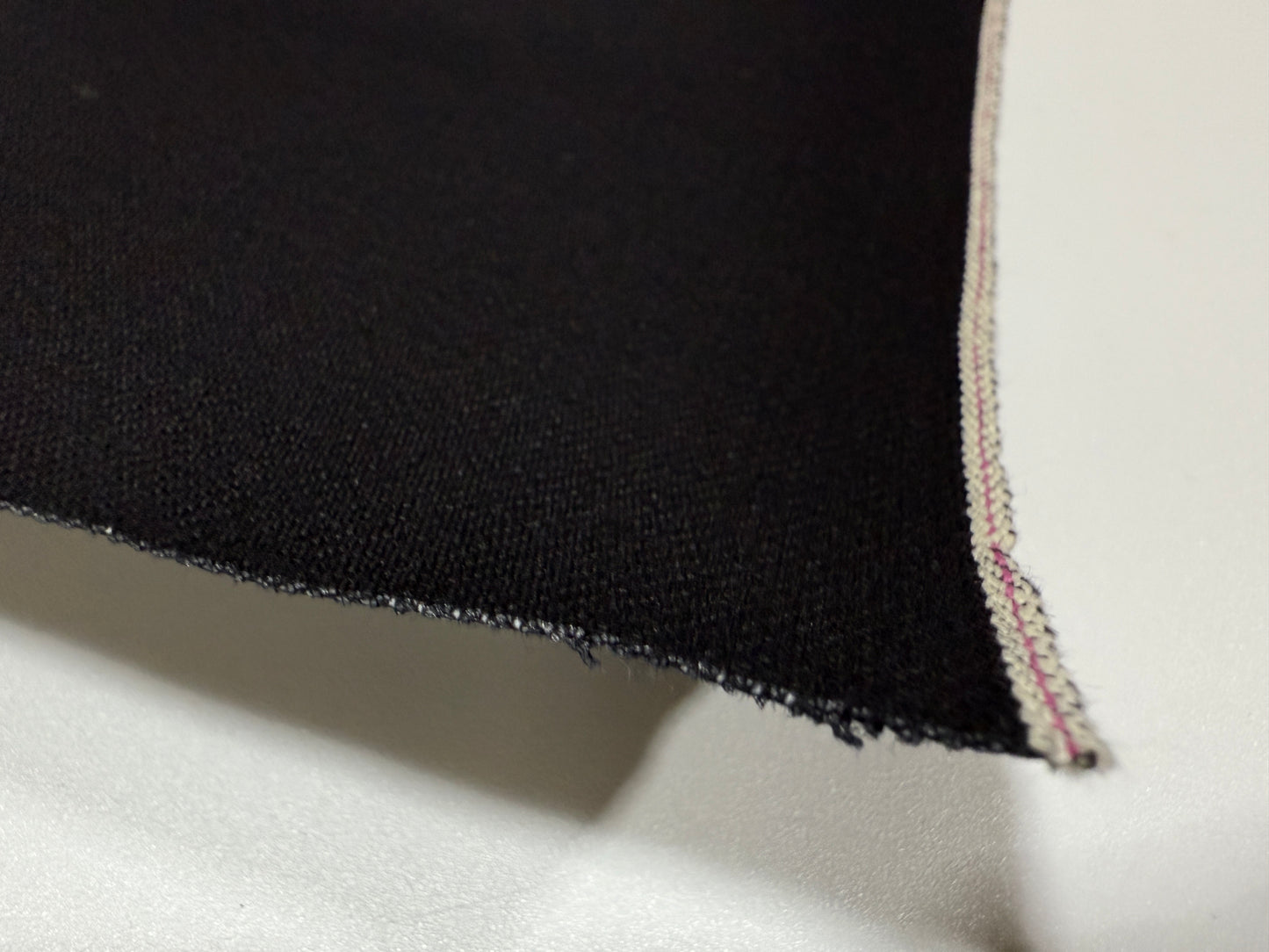 Okayama Denim | Close-up of 14.6 oz double-sided black Japanese selvage fabric showing smooth texture and edge detail.