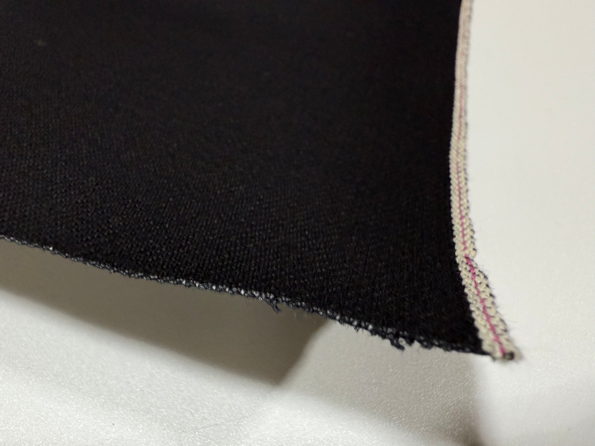 Okayama Denim | Close-up of 14.6 oz double-sided black Japanese selvage fabric showing smooth texture and edge detail.