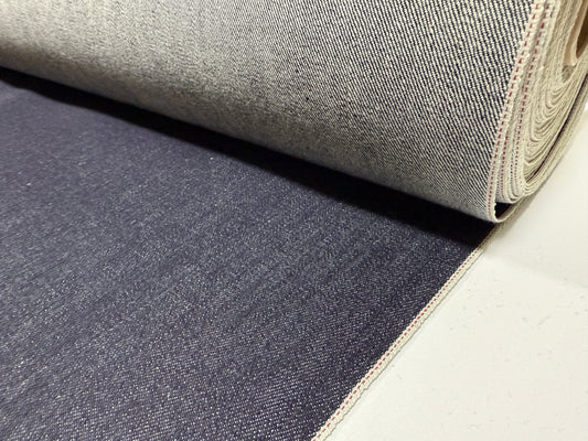 Okayama Denim 13.5 oz indigo Japanese selvage denim fabric rolled out, showing texture and color details.