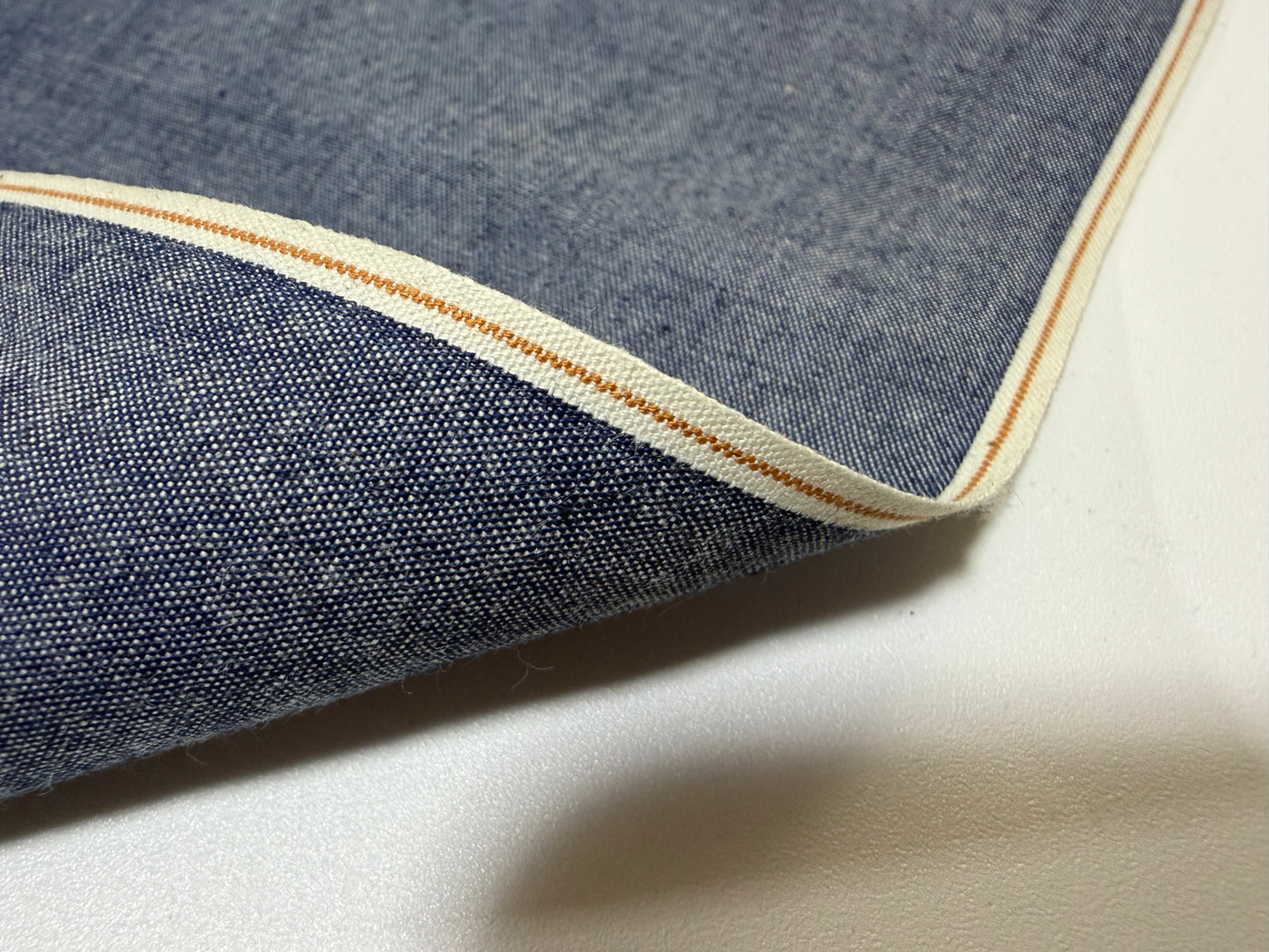 Okayama Denim - Close-up of 4.5 oz Japanese indigo selvage chambray fabric showcasing its unique selvedge edge.