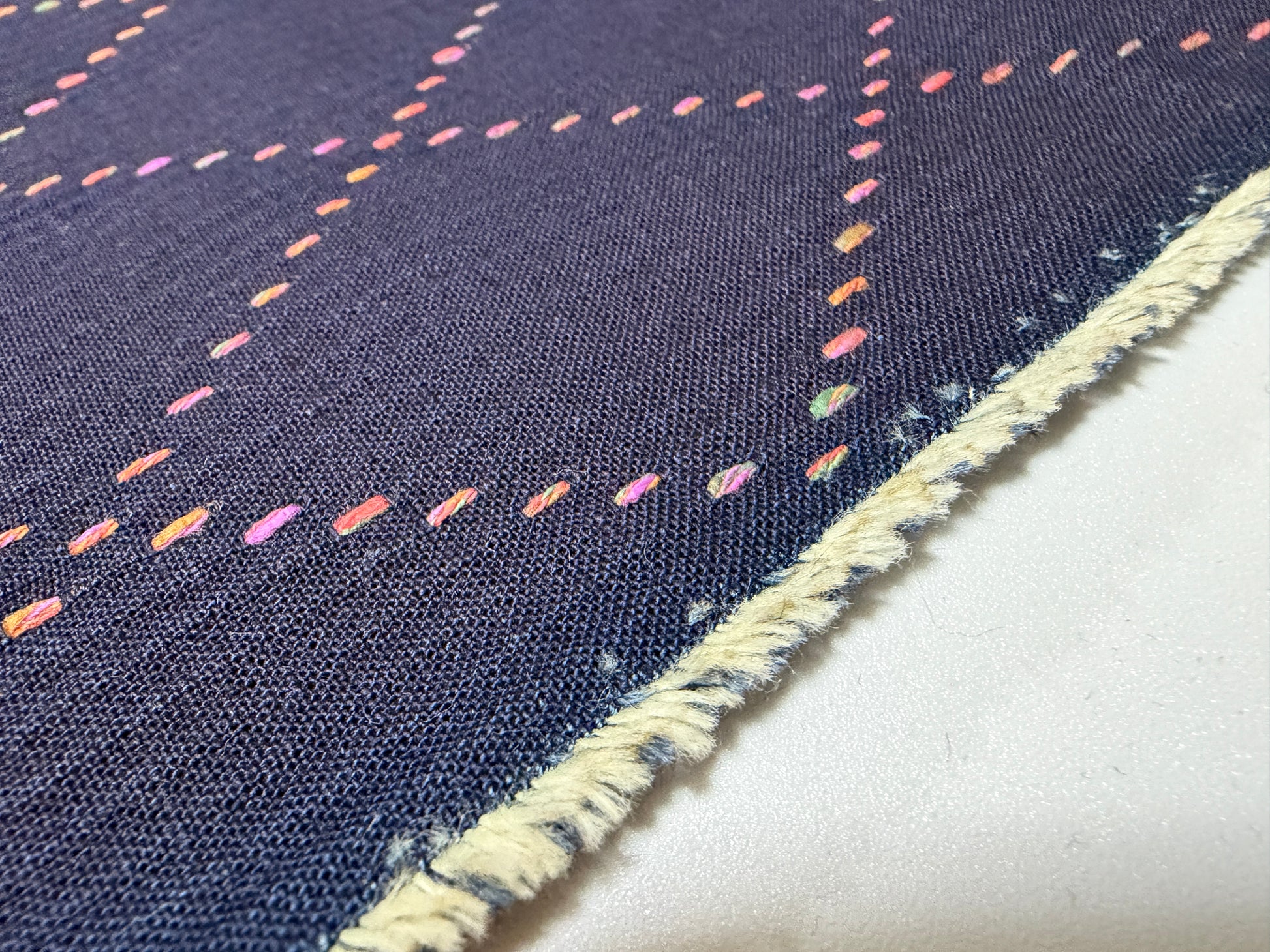 Okayama Denim 7 oz Sashiko fabric with colorful multi-color stitching and frayed edge detail.