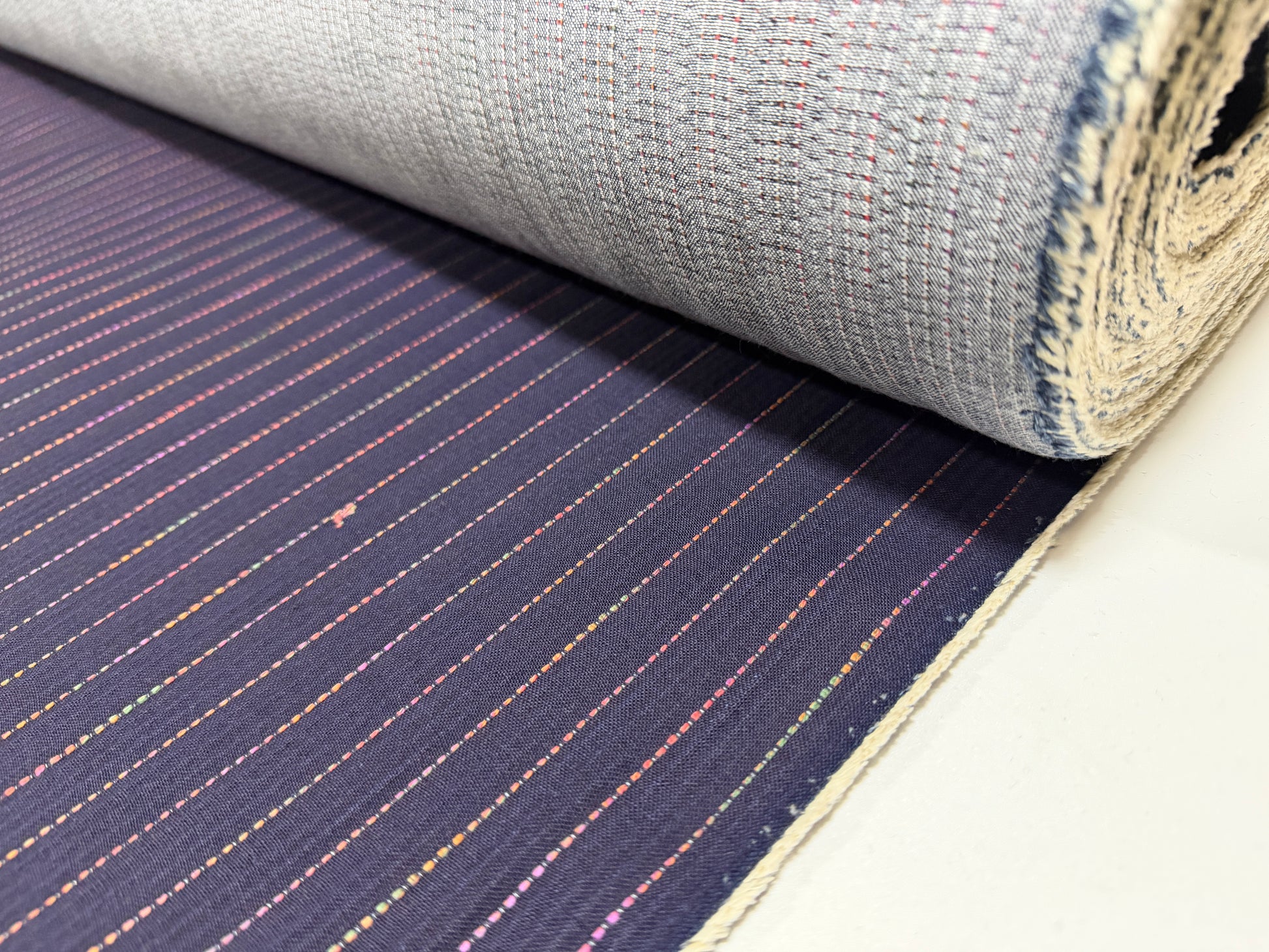 Okayama Denim 7 oz Sashiko Stripes Cotton Fabric with colorful stitching pattern rolled up on a table.