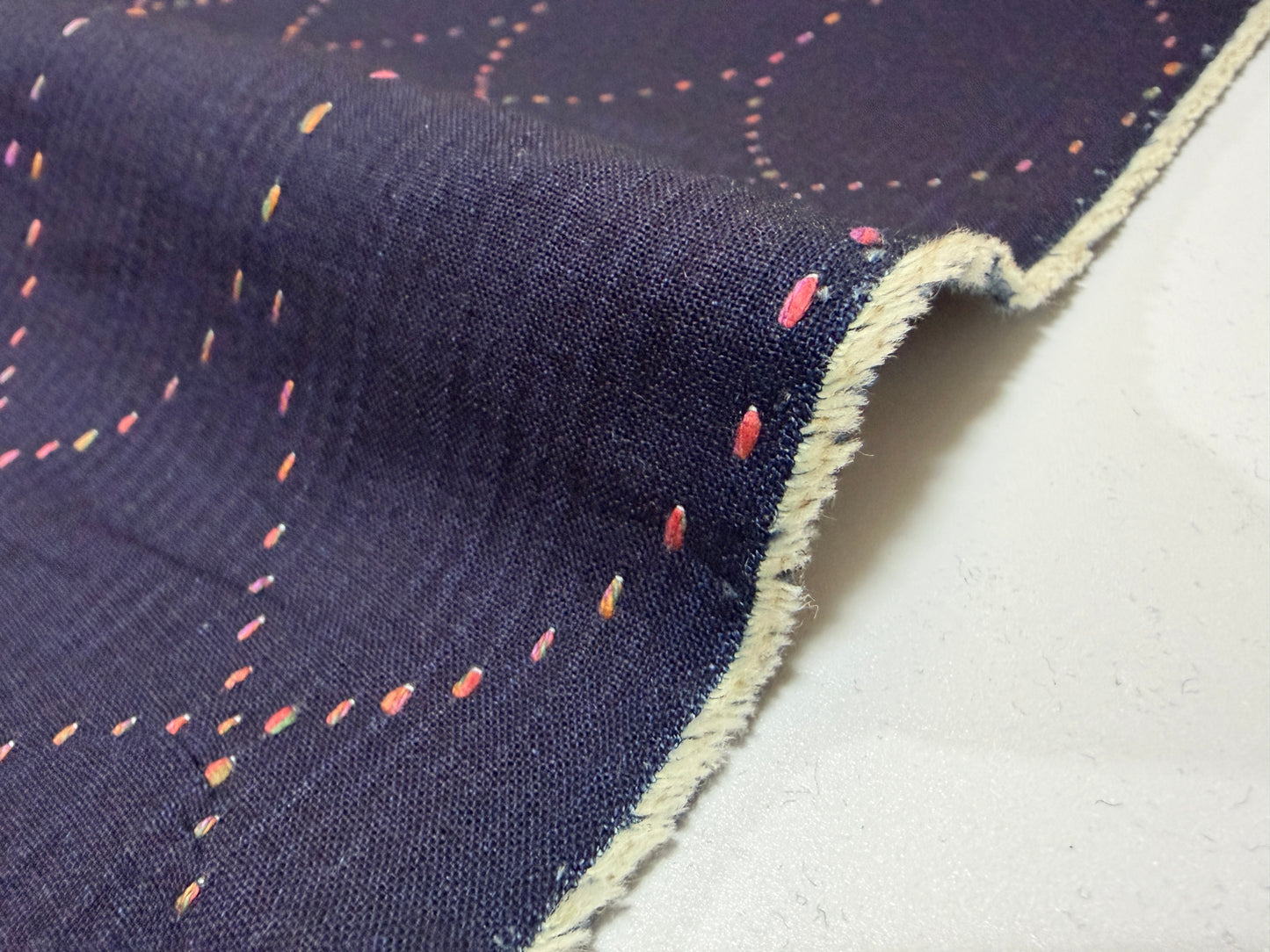 Okayama Denim 7 oz Sashiko Diamond Lattice cotton fabric showing colorful stitching detail on a dark background.