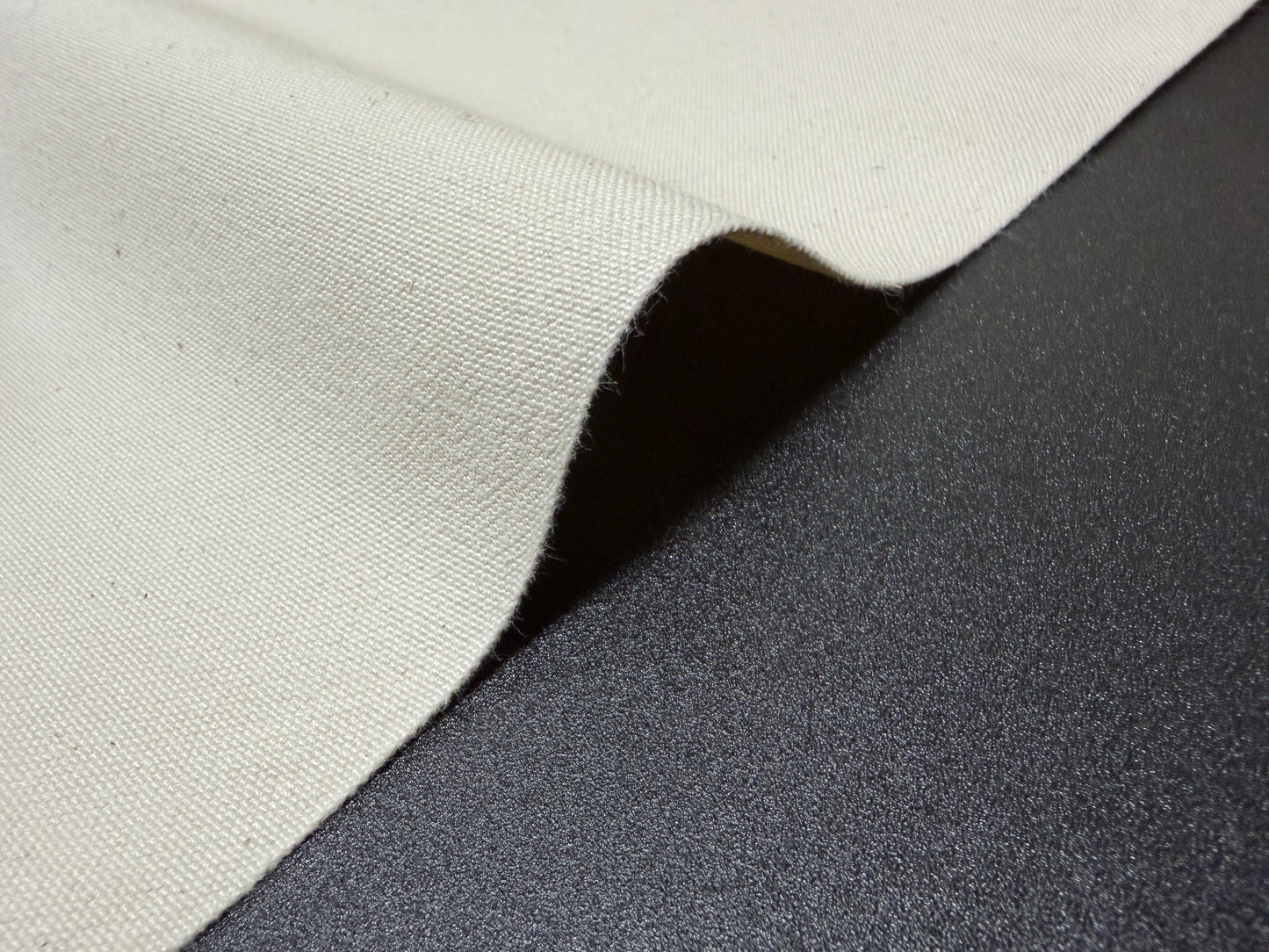 Okayama Denim 10 oz Japanese Cotton Ecru Color Canvas fabric lying on a dark surface.