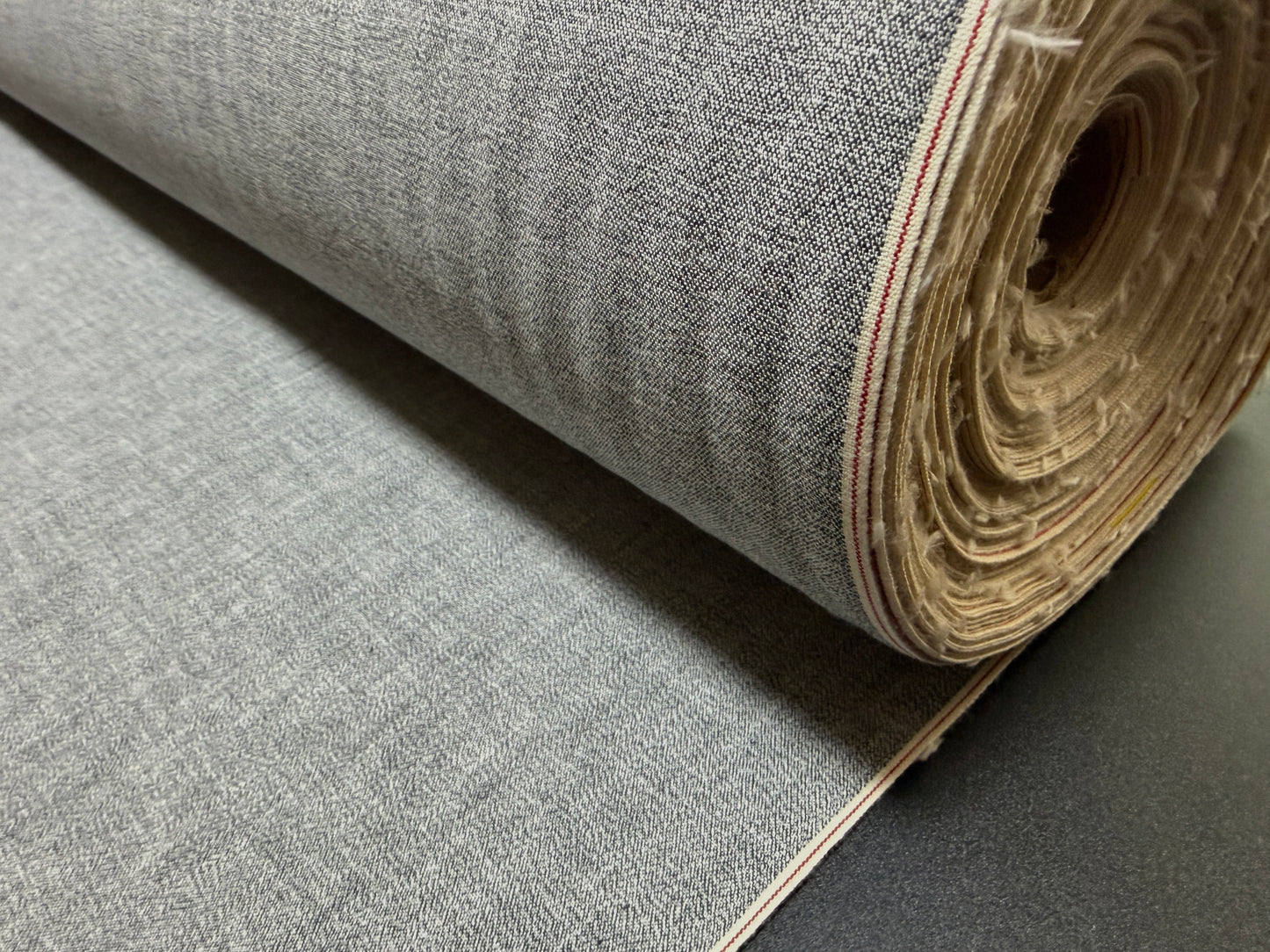 Okayama Denim 6 oz Japanese Gray chambray fabric with red selvage rolled up for purchase.