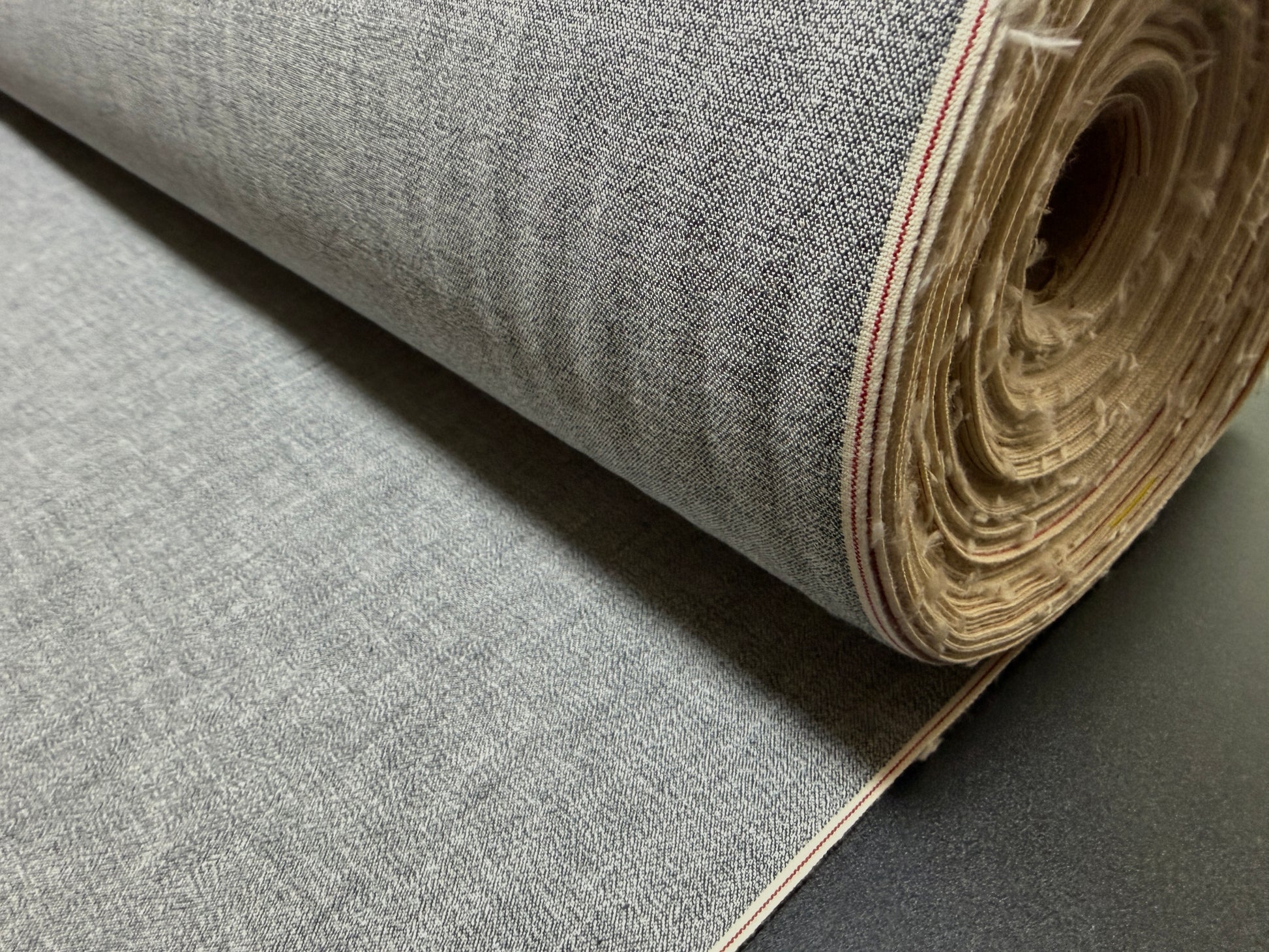 Okayama Denim 6 oz Japanese Gray chambray fabric with red selvage rolled up for purchase.