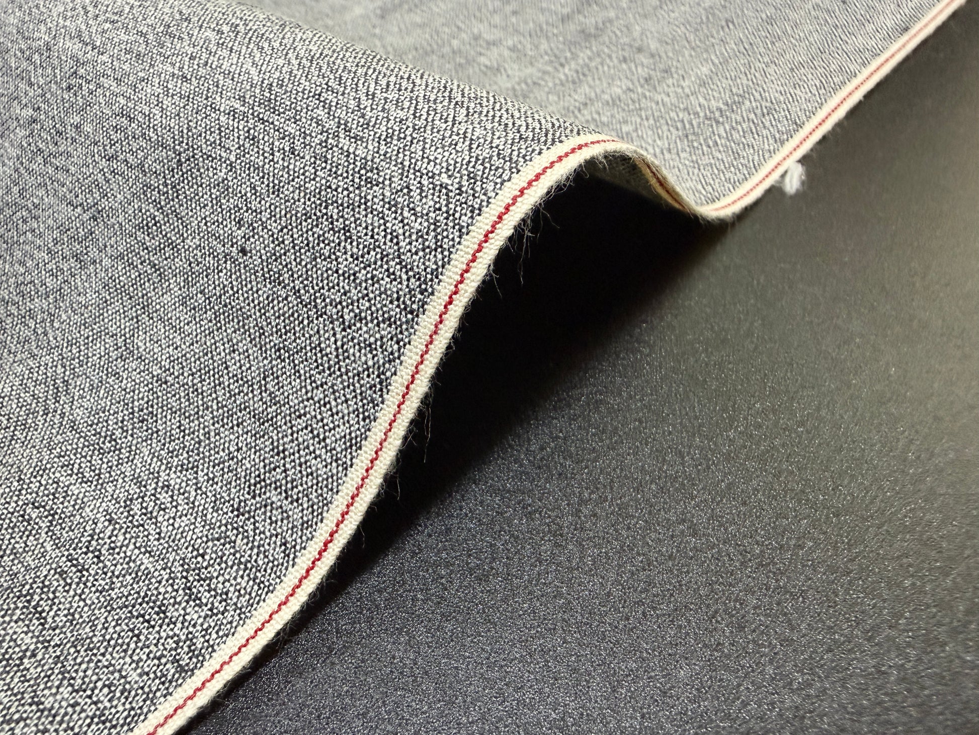 Okayama Fabric | 6 oz Japanese Gray Chambray with Red Selvage detail on black background.