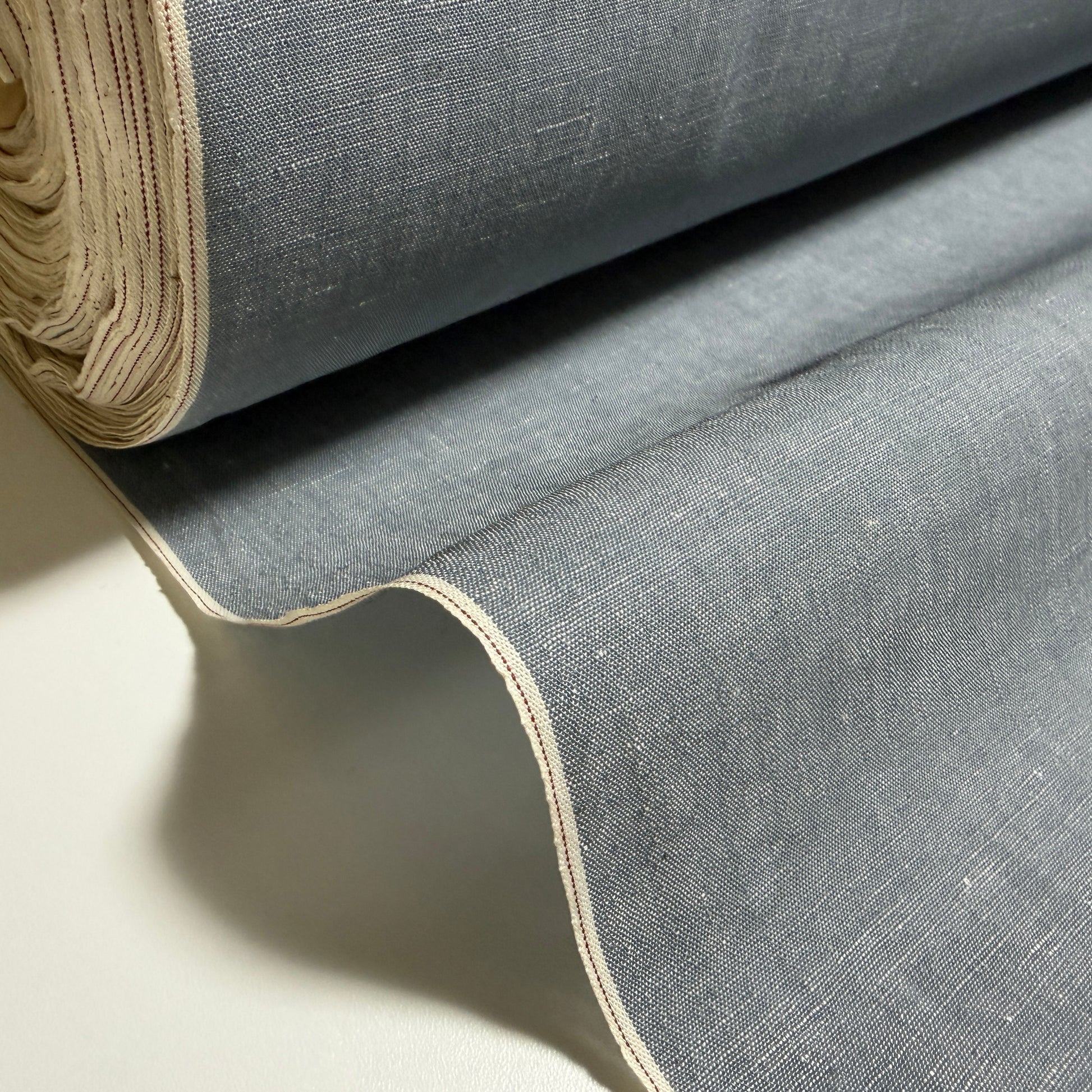 Okayama Denim grayish-blue slub chambray fabric with red selvage displayed in a rolled yard.