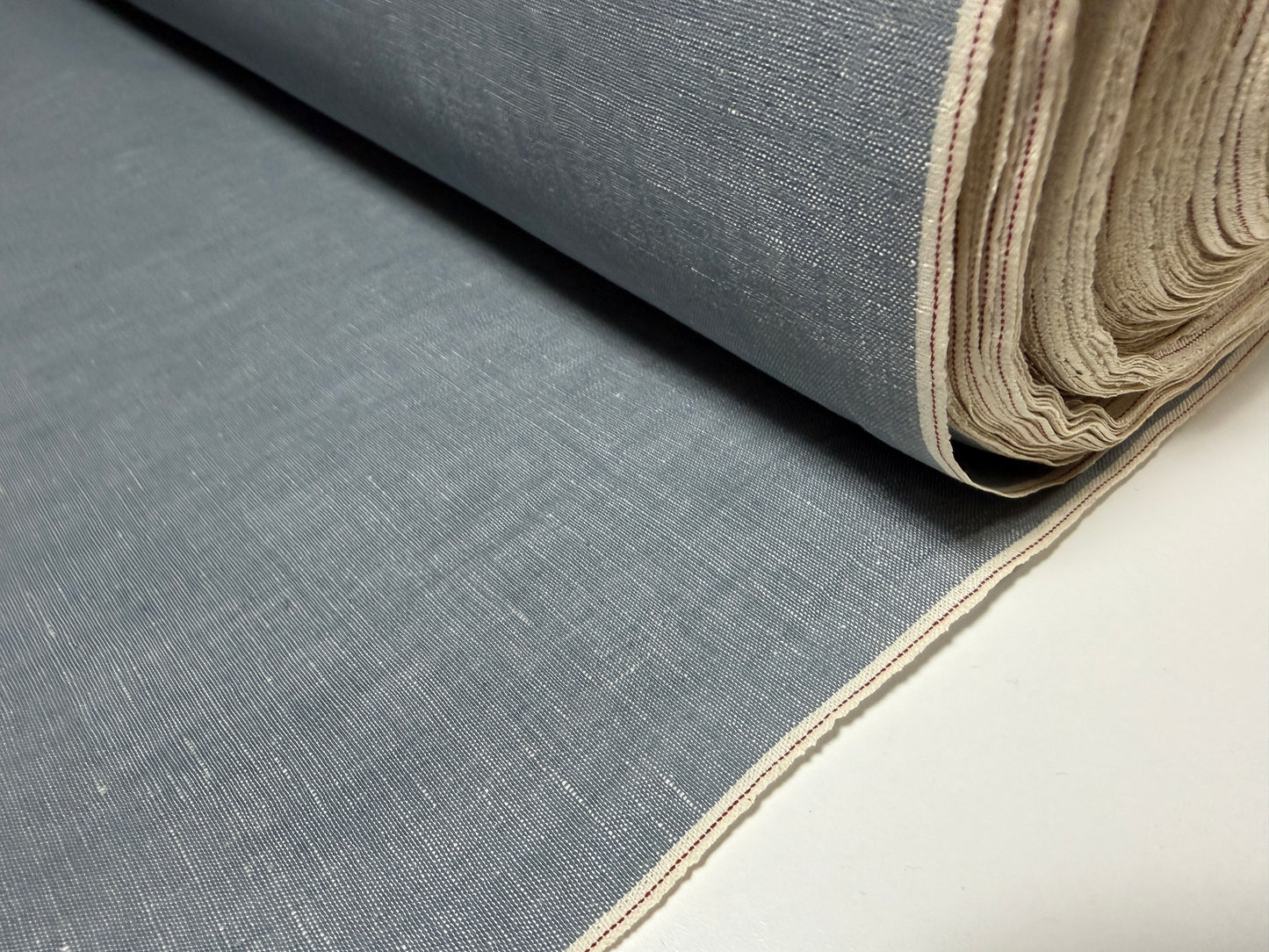 Okayama Denim grayish-blue slub chambray fabric rolled up with red selvage detail.