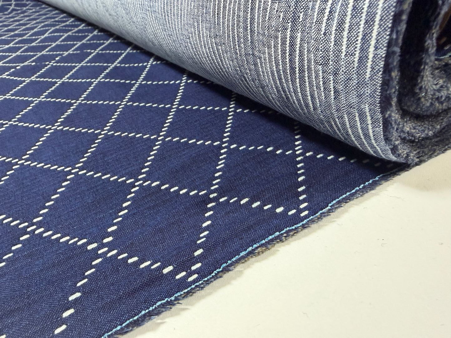 Okayama Denim fabric showcasing 7 oz blue & white Sashiko stitching pattern rolled on a table.