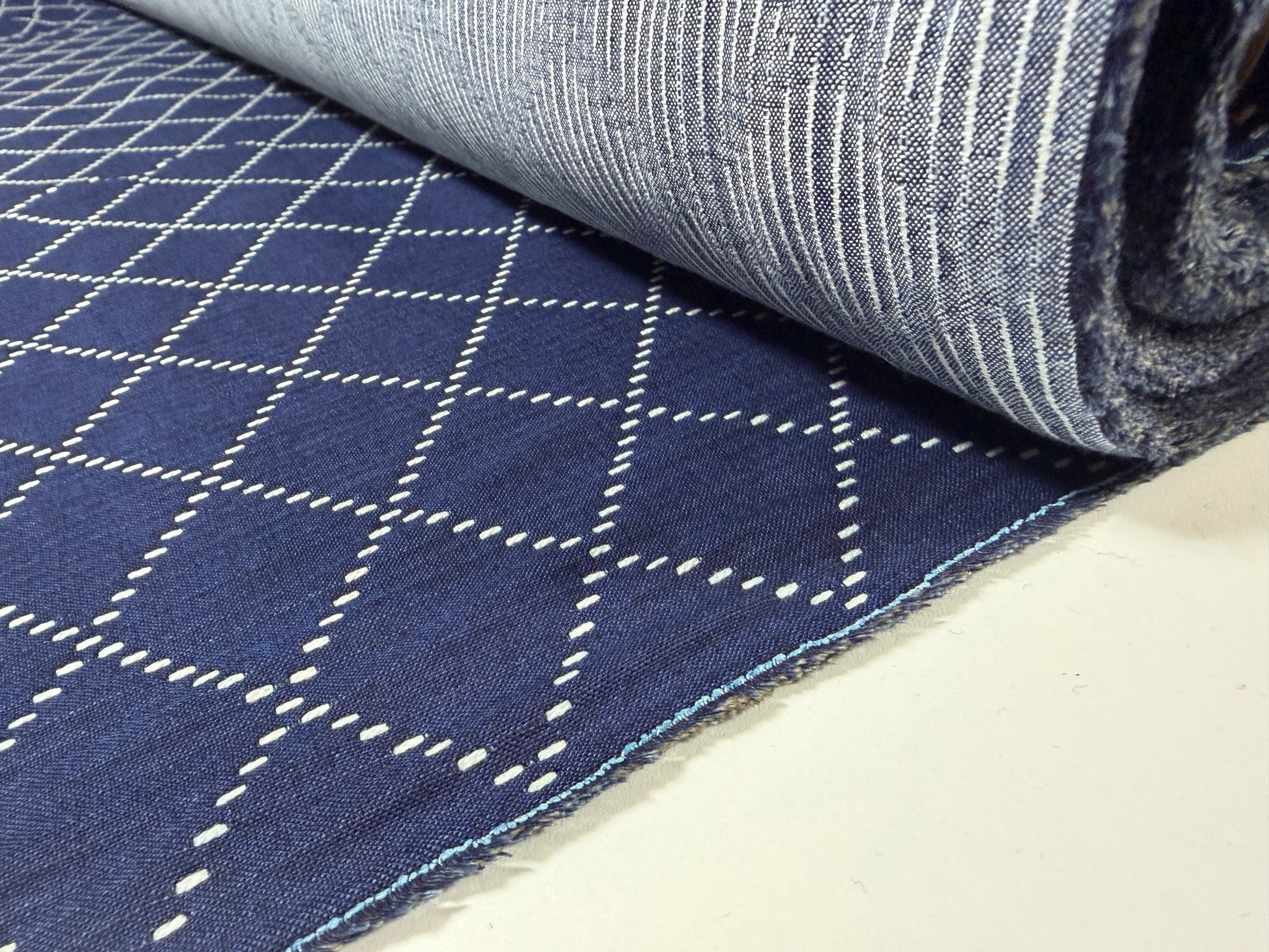 Okayama Denim fabric showcasing 7 oz blue & white Sashiko stitching pattern rolled on a table.