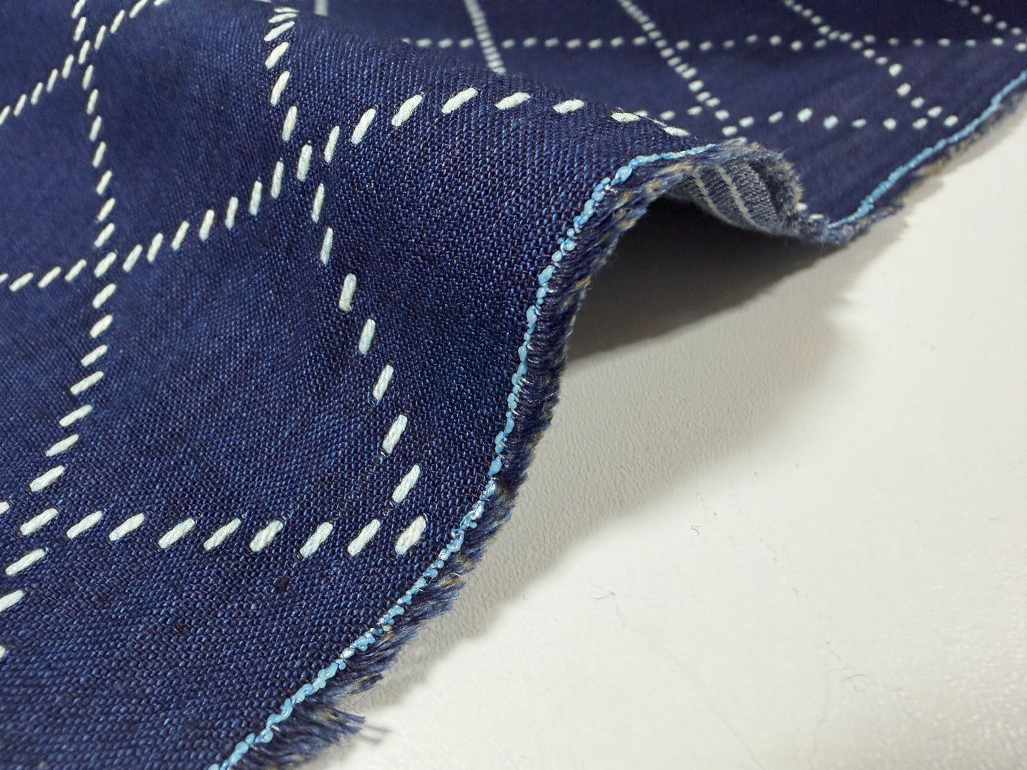 Okayama Denim fabric showcasing blue and white sashiko stitching with a close-up view of the textured edge.