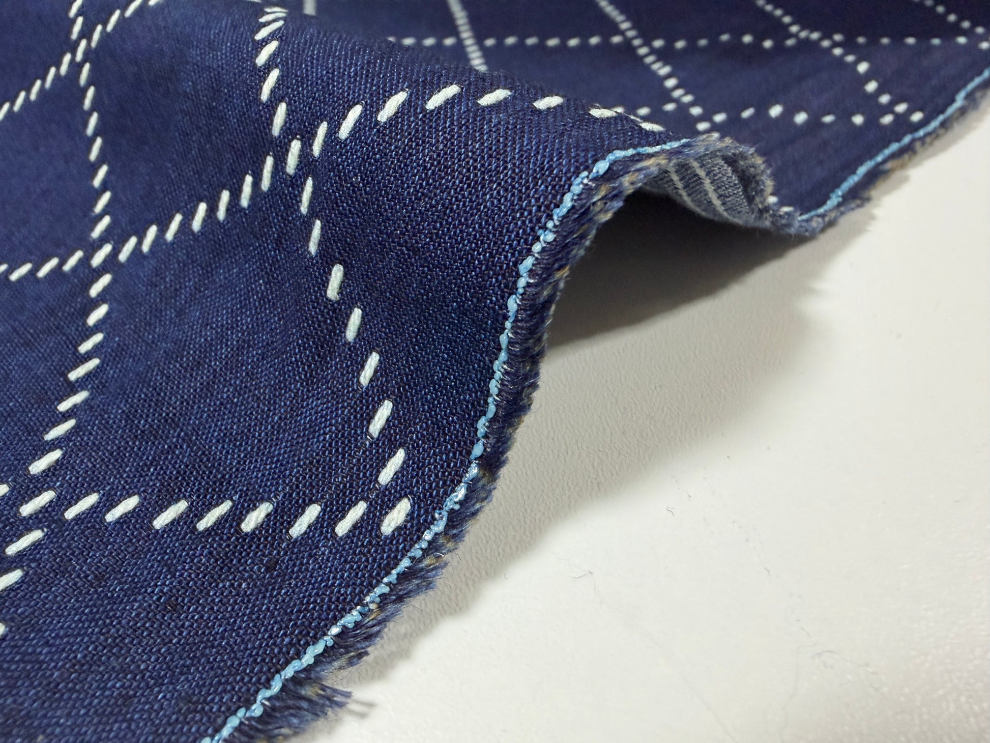 Okayama Denim fabric showcasing blue and white sashiko stitching with a close-up view of the textured edge.