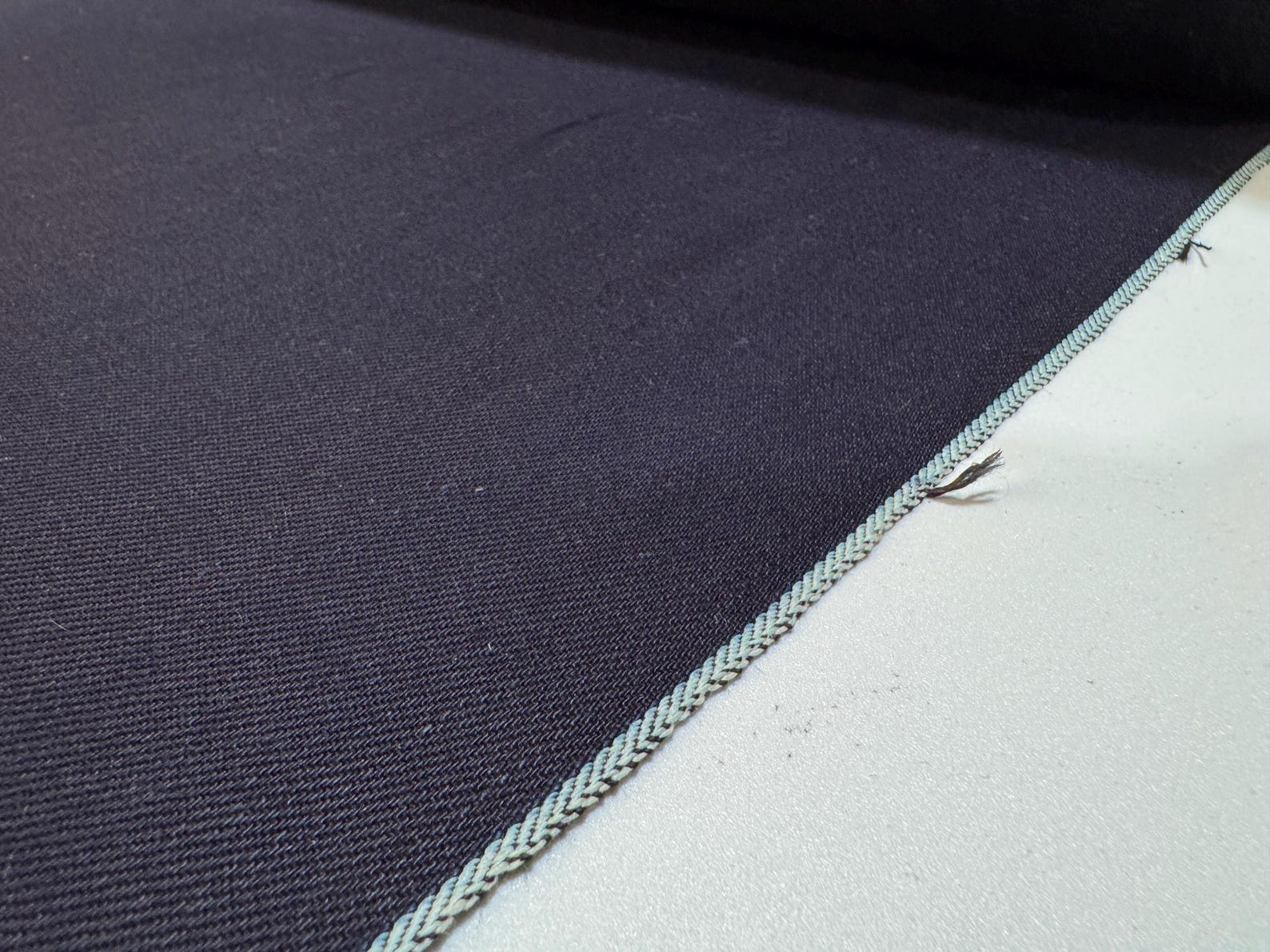 Close-up of Okayama Denim, 12 oz double-sided indigo selvage fabric showcasing the smooth navy blue texture and edge details.