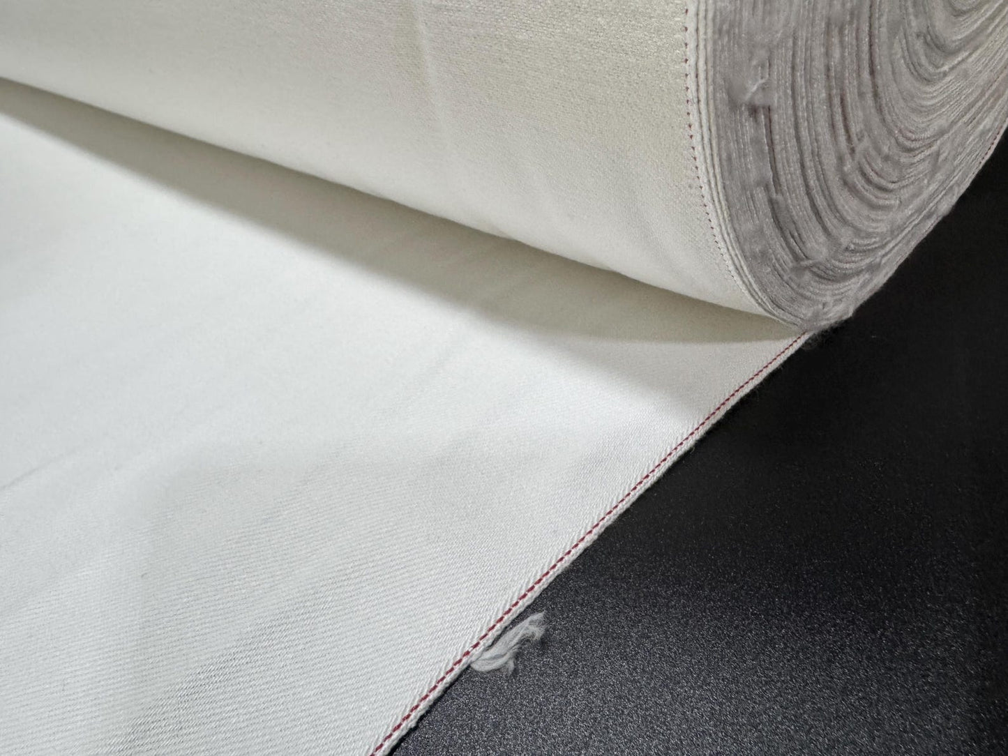 Okayama Denim 13 oz White Selvedge fabric with red edge rolled on a black surface.