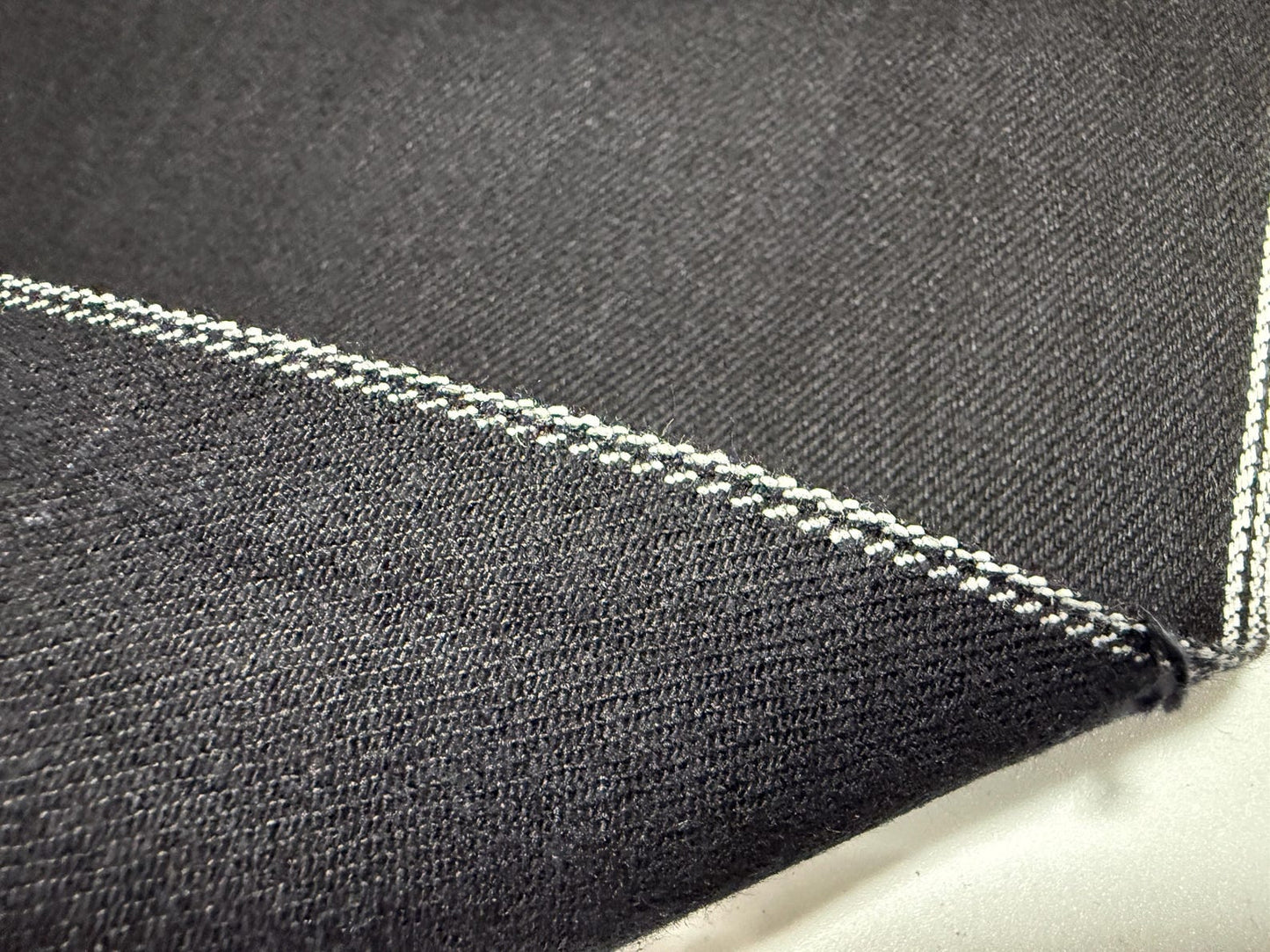 Okayama Denim 11oz double-sided black Japanese selvage fabric showcasing smooth texture and distinctive stitching.