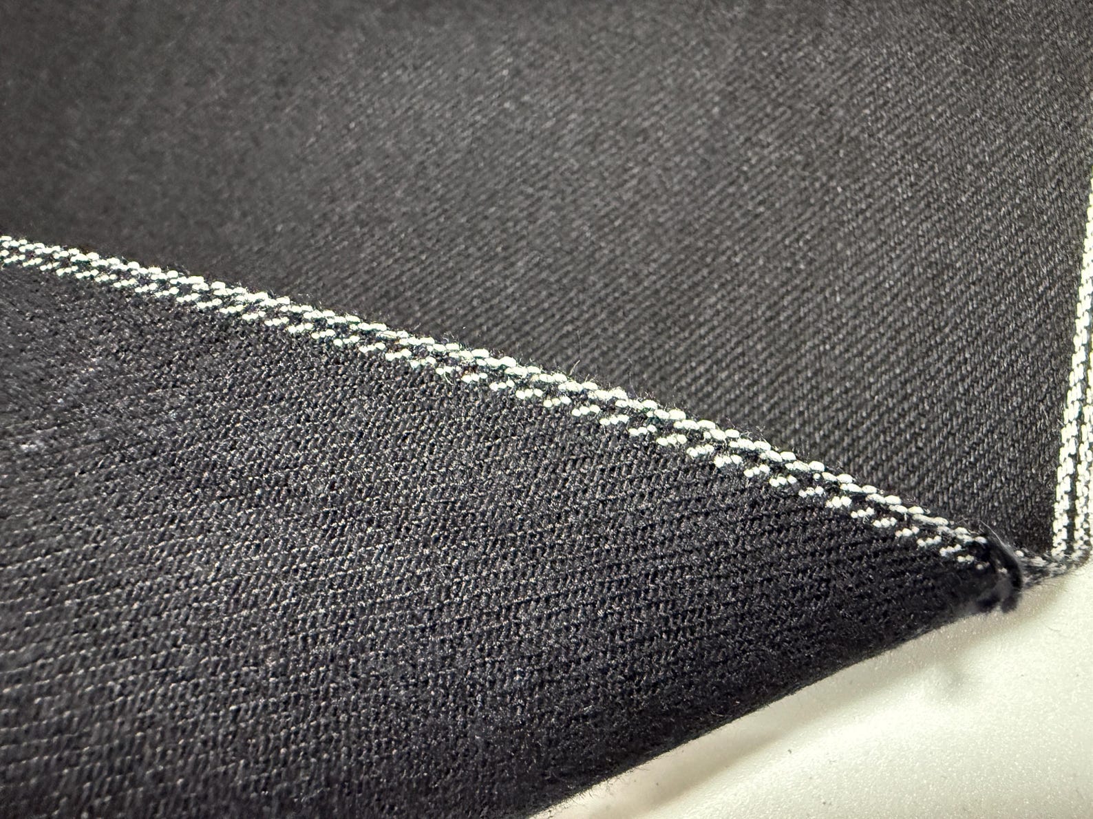 Okayama Denim 11oz double-sided black Japanese selvage fabric showcasing smooth texture and distinctive stitching.