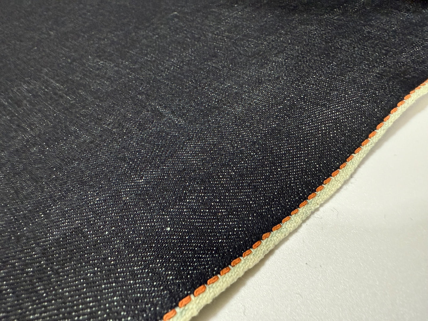 Okayama Denim | Close-up of 13.5 oz indigo Japanese selvedge denim fabric with thick orange selvage detail.
