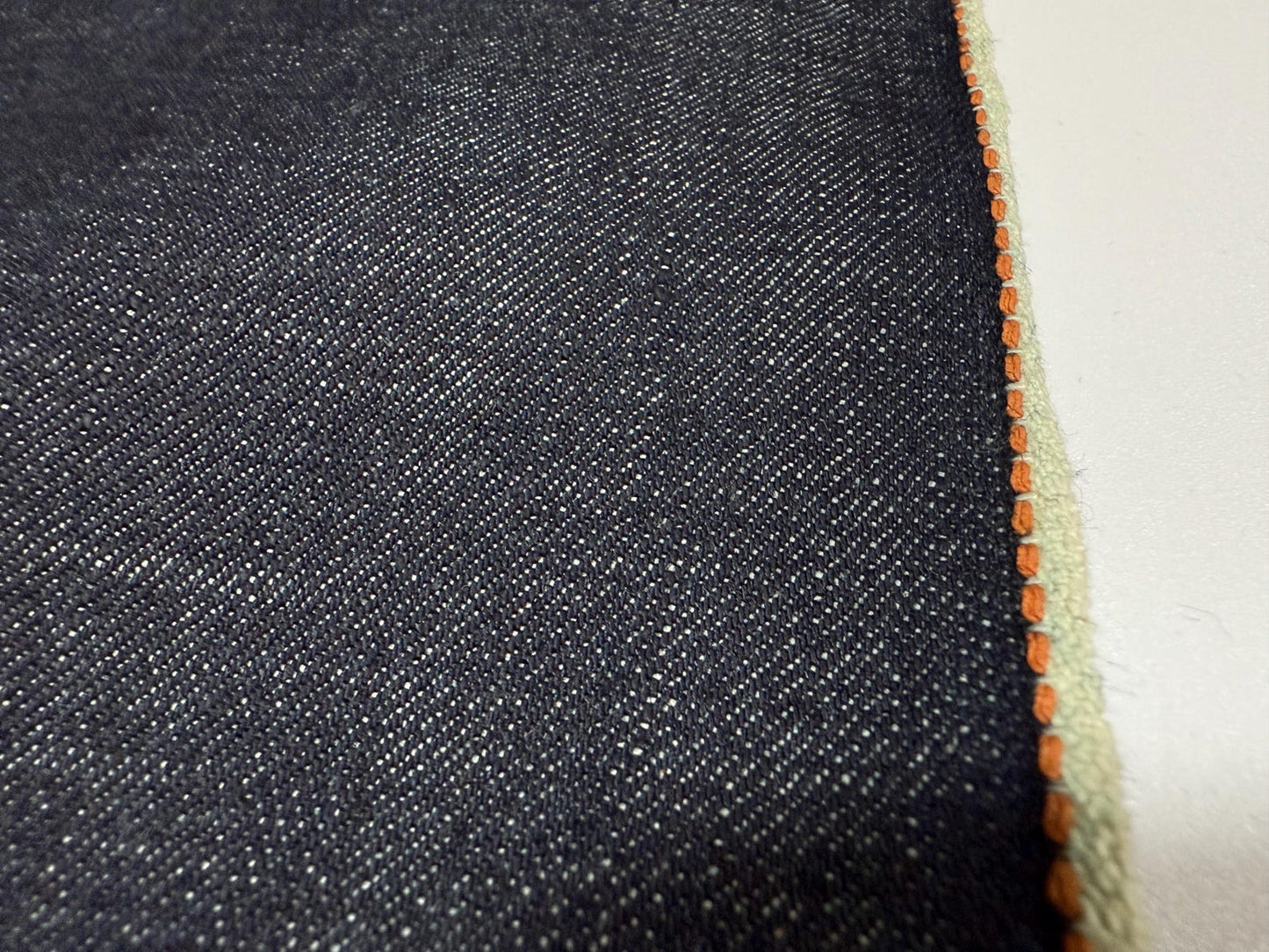 Okayama Denim fabric showing 13.5 oz indigo Japanese selvage with thick orange selvage stitching.