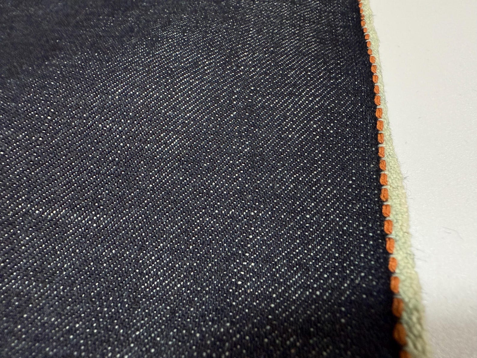 Okayama Denim fabric showing 13.5 oz indigo Japanese selvage with thick orange selvage stitching.