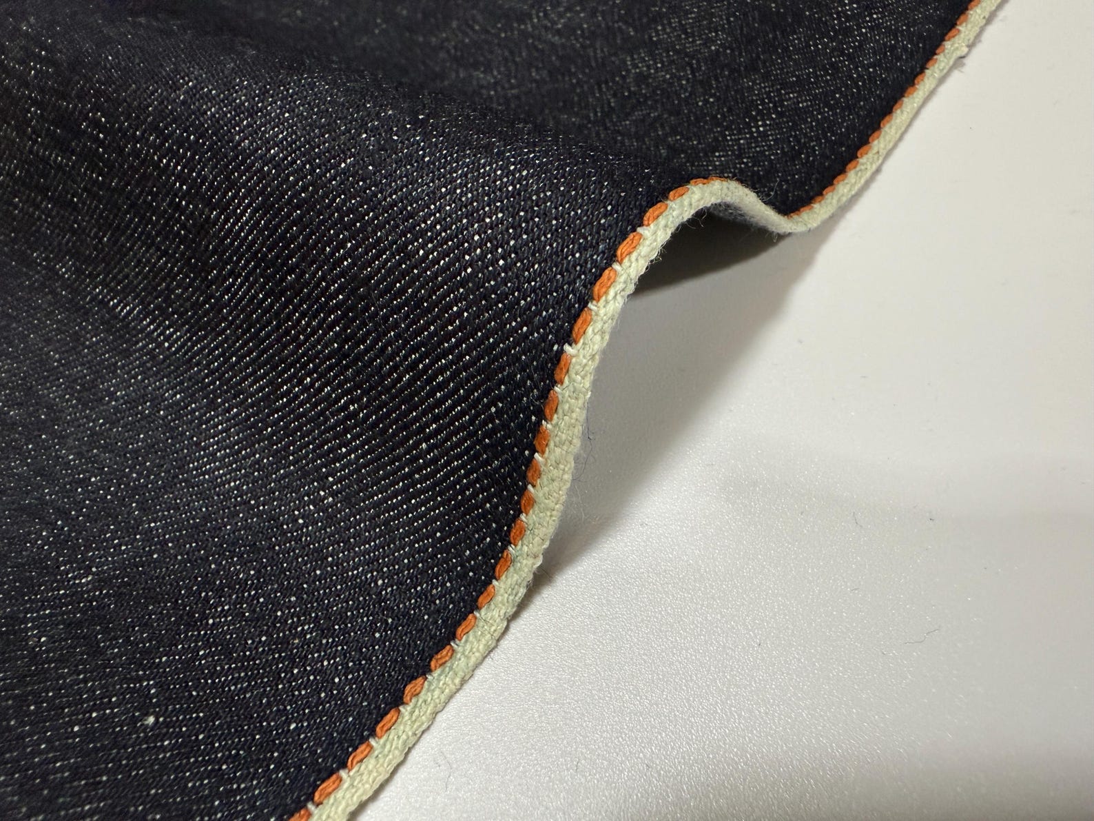 Okayama Denim | Close-up of 13.5 oz indigo denim fabric with thick orange selvage edge.