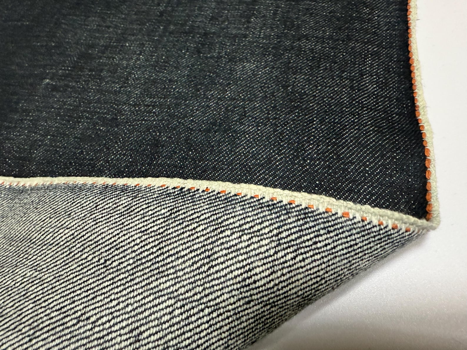 Okayama Denim | 13.5 oz indigo Japanese selvage denim fabric showing thick orange selvage edge detail.