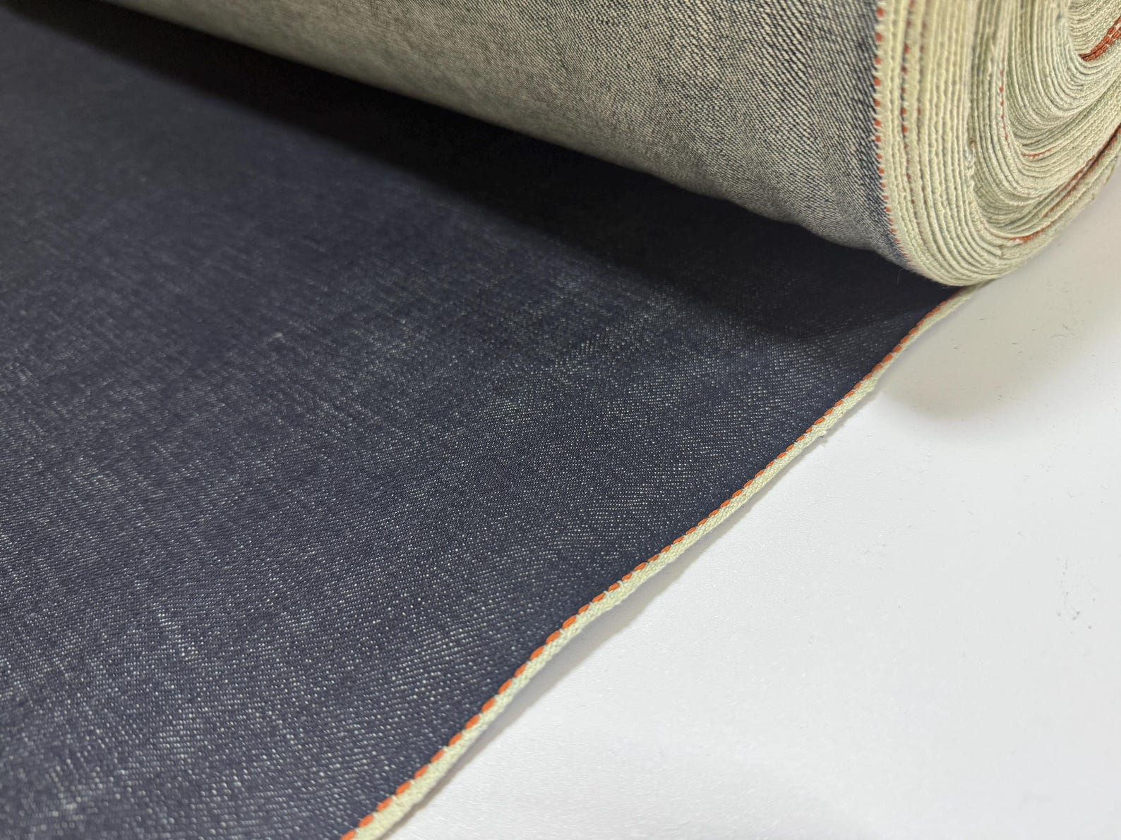 Okayama Denim 13.5 oz indigo Japanese selvage denim fabric rolled up with thick orange selvage edge.