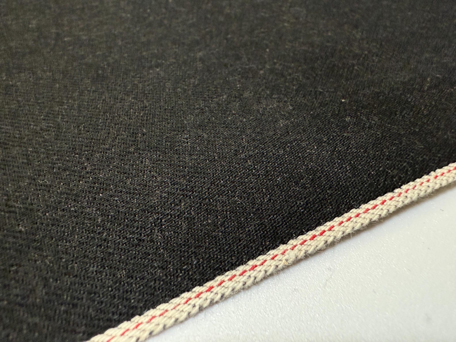 Texture of Okayama Denim | 13.5 oz black selvage Japanese denim with visible edge stitching.
