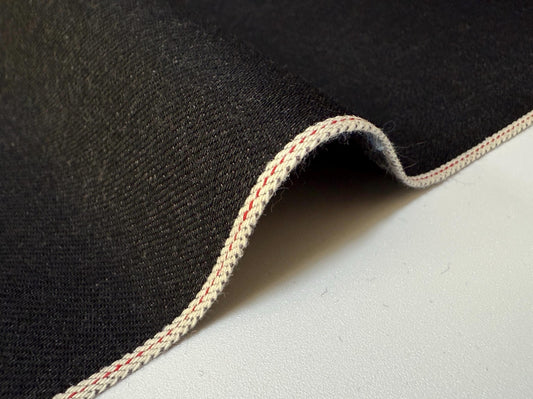 Okayama Denim 13.5 oz black/gray selvage Japanese denim fabric showing smooth texture and red selvage stitching.